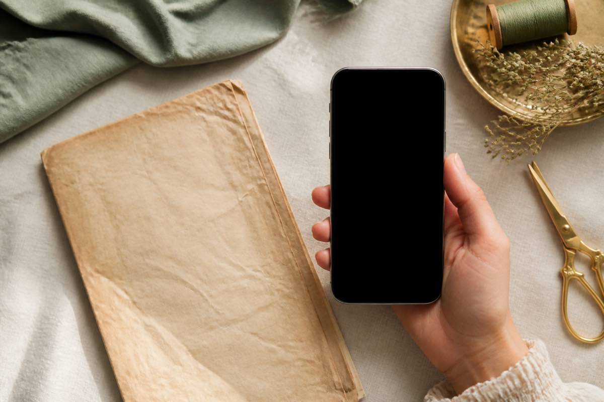 A phone held over a sewing pattern envelope to photograph it into the studio catalog